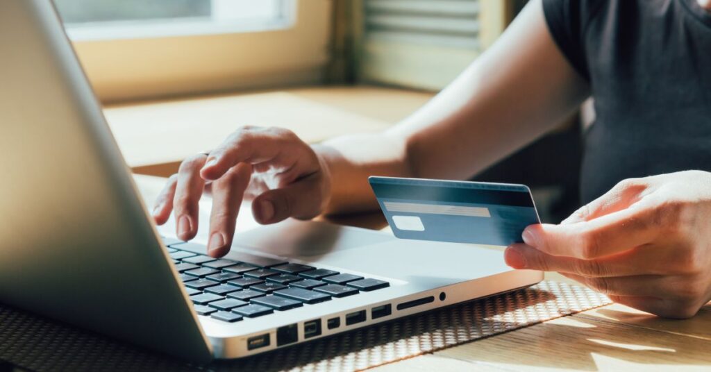A person's hand is holding a credit card while the other hand is typing on the keyboard of a laptop.