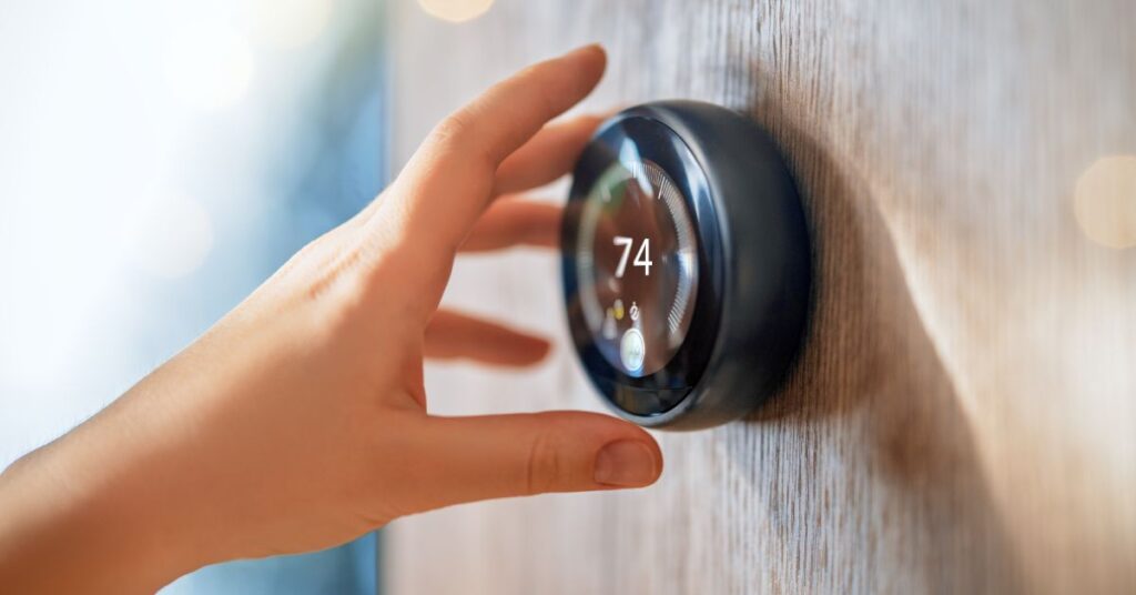 A person's left hand is reaching out to touch a black, modern, circular thermostat that reads "74."