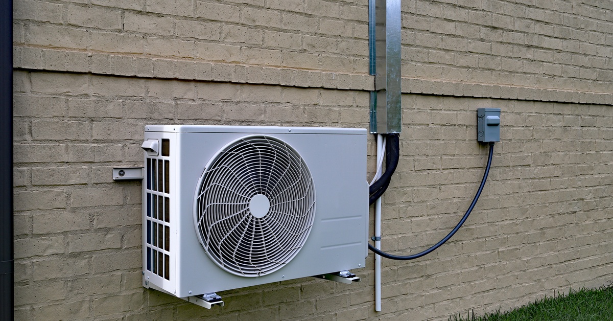 Exterior mini-split condenser unit mounted beside a home’s brick wall, with piping connected and visible.