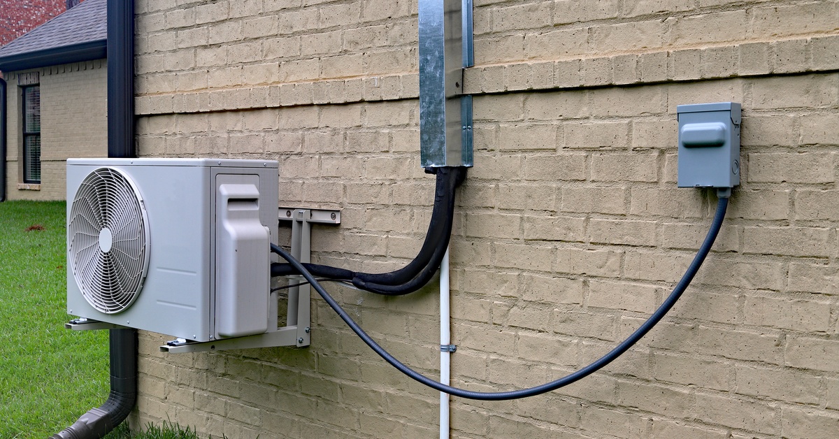Outdoor mini-split condenser unit installed beside a brick exterior wall, with connected lines and mounting hardware.
