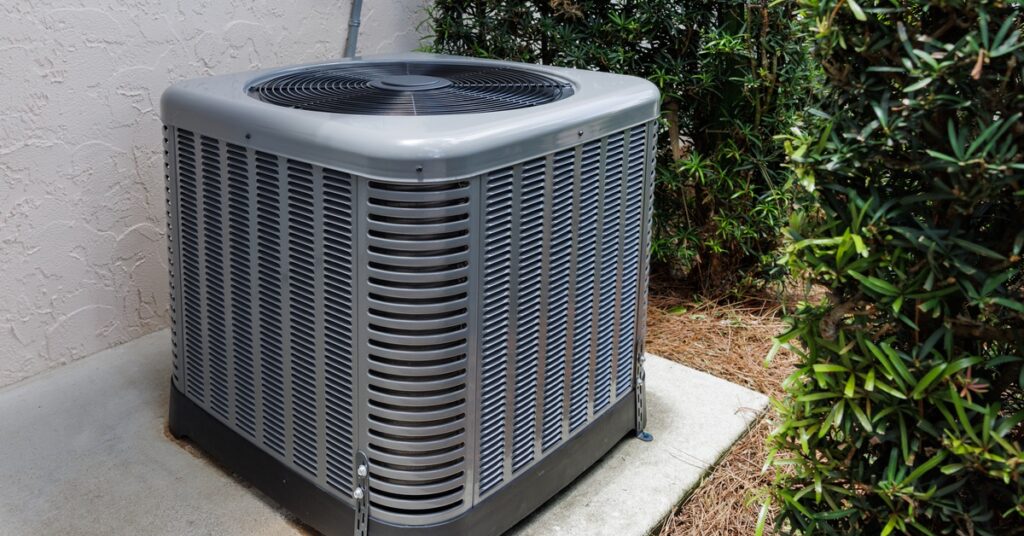 Modern outdoor HVAC air conditioner unit on a concrete slab beside a house next to grass and exterior siding.
