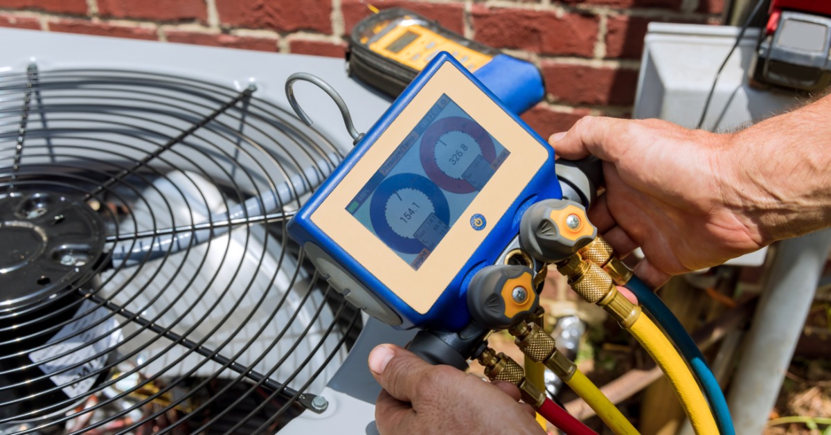 Technician checking an outdoor air conditioner with gauges during refrigerant leak detection and service.
