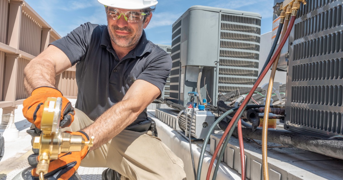 HVAC technician wearing protective gear repairs an outdoor air conditioner unit during a service visit.