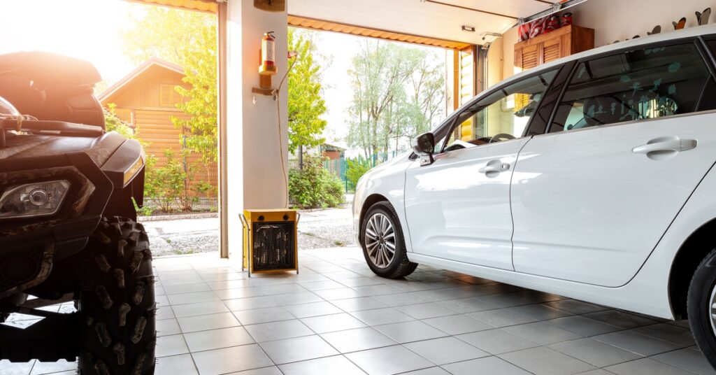 a double garage with a parked car, ATV, wooden shelves, tools, equipment, and sunlight entering open doors.