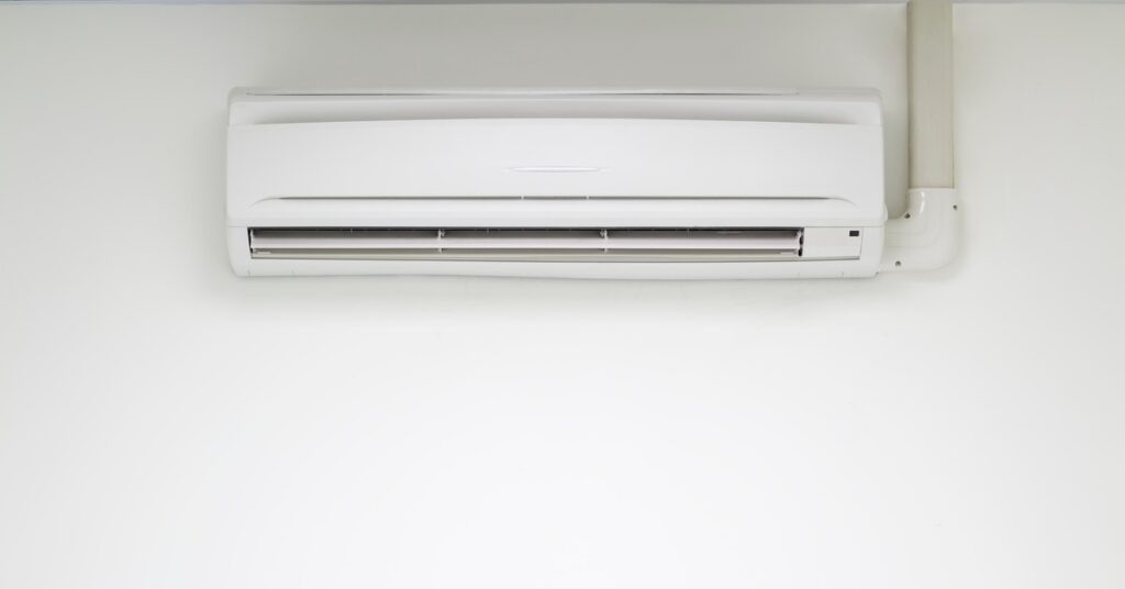 a white wall-mounted indoor air conditioner above a floor, with a remote control and a power cord nearby.