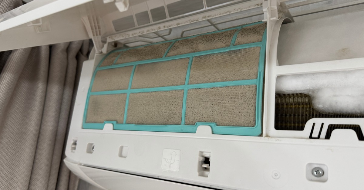 A dusty air conditioner filter with a turquoise frame beside white ice buildup inside an open indoor unit.