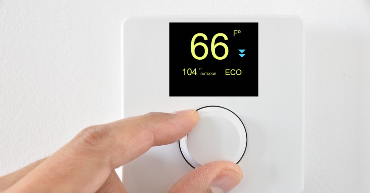 A hand turning a white wall thermostat dial below a digital screen showing 66 degrees, 104 outdoor, and ECO.