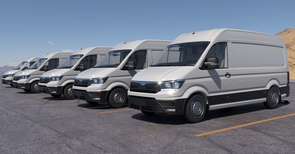 A row of white cargo vans parked in an outdoor lot under a blue sky.