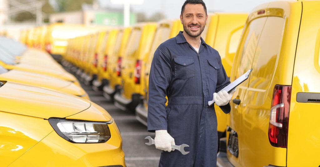 A man holding a clipboard and wrench between rows of yellow delivery vans.