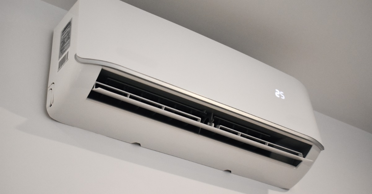 A white wall-mounted air conditioner with open vents and a lit temperature display installed near the ceiling.